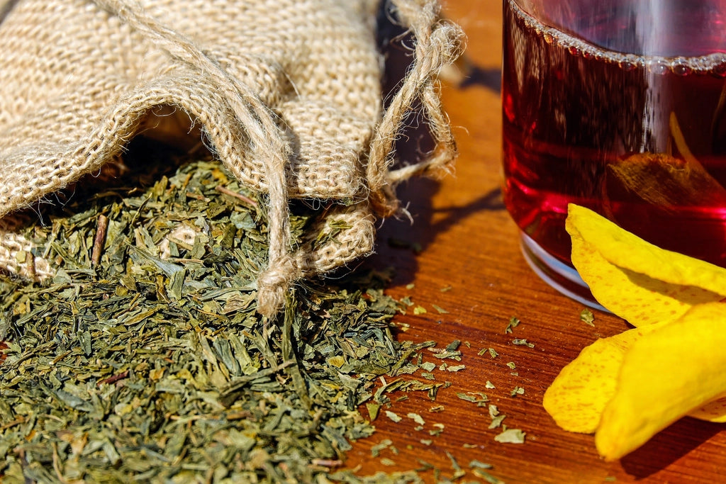Loose dried herbs spilling from a burlap sack beside a glass of herbal tea